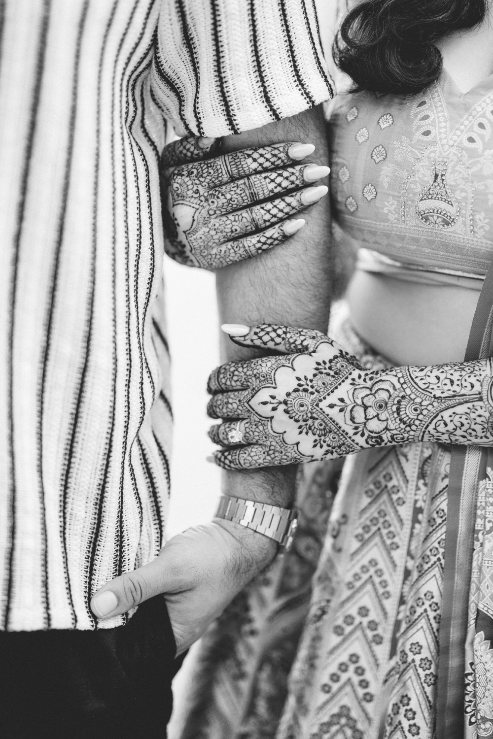 A couple in traditional South Asian wedding attire, hands detailed with bridal mehndi